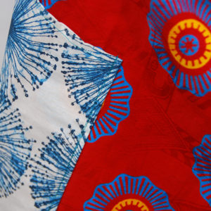 Tablier en belle wax rouge au motifs bleu et orange avec poches à motif bleu sur fond blanc.