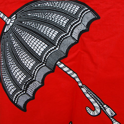 Tablier en wax rouge avec motifs noir et blanc en forme d'ombrelles.